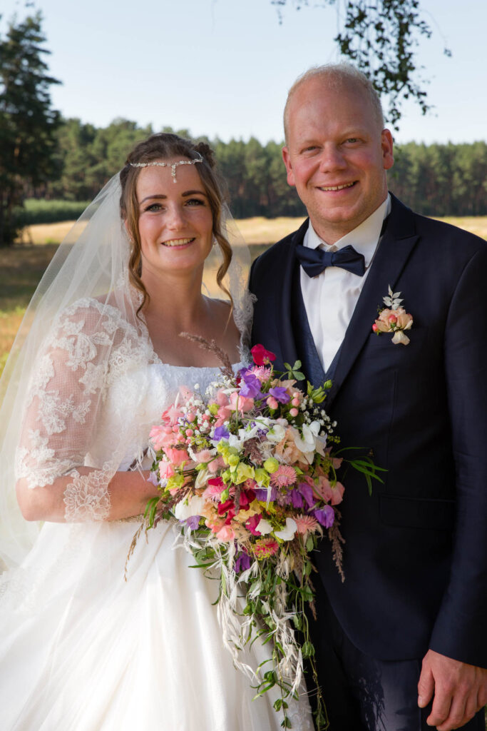 Brautpaar mit Brautstrauß unter Baum auf Feld.