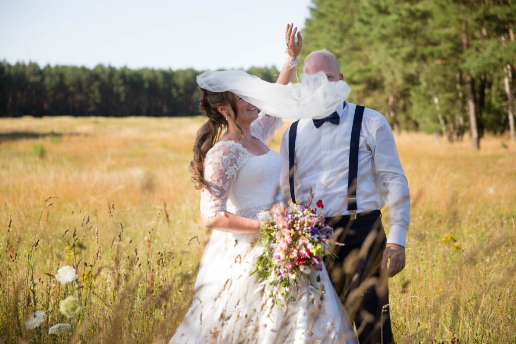 Braut mit Schleier und Bräutigam auf Feld im Sommer.