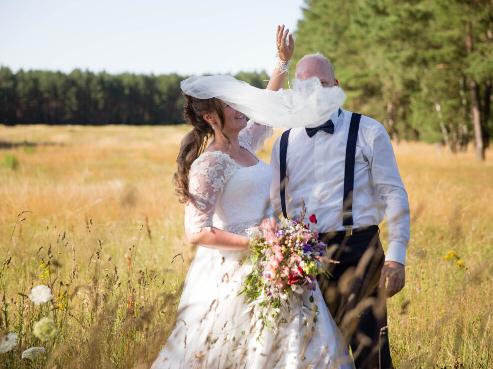 Braut mit Schleier und Bräutigam auf Feld im Sommer.