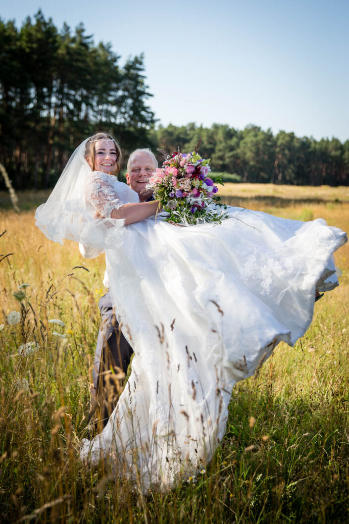 Bräutigam hält Braut auf dem Arm, ein Feld im Sommer.
